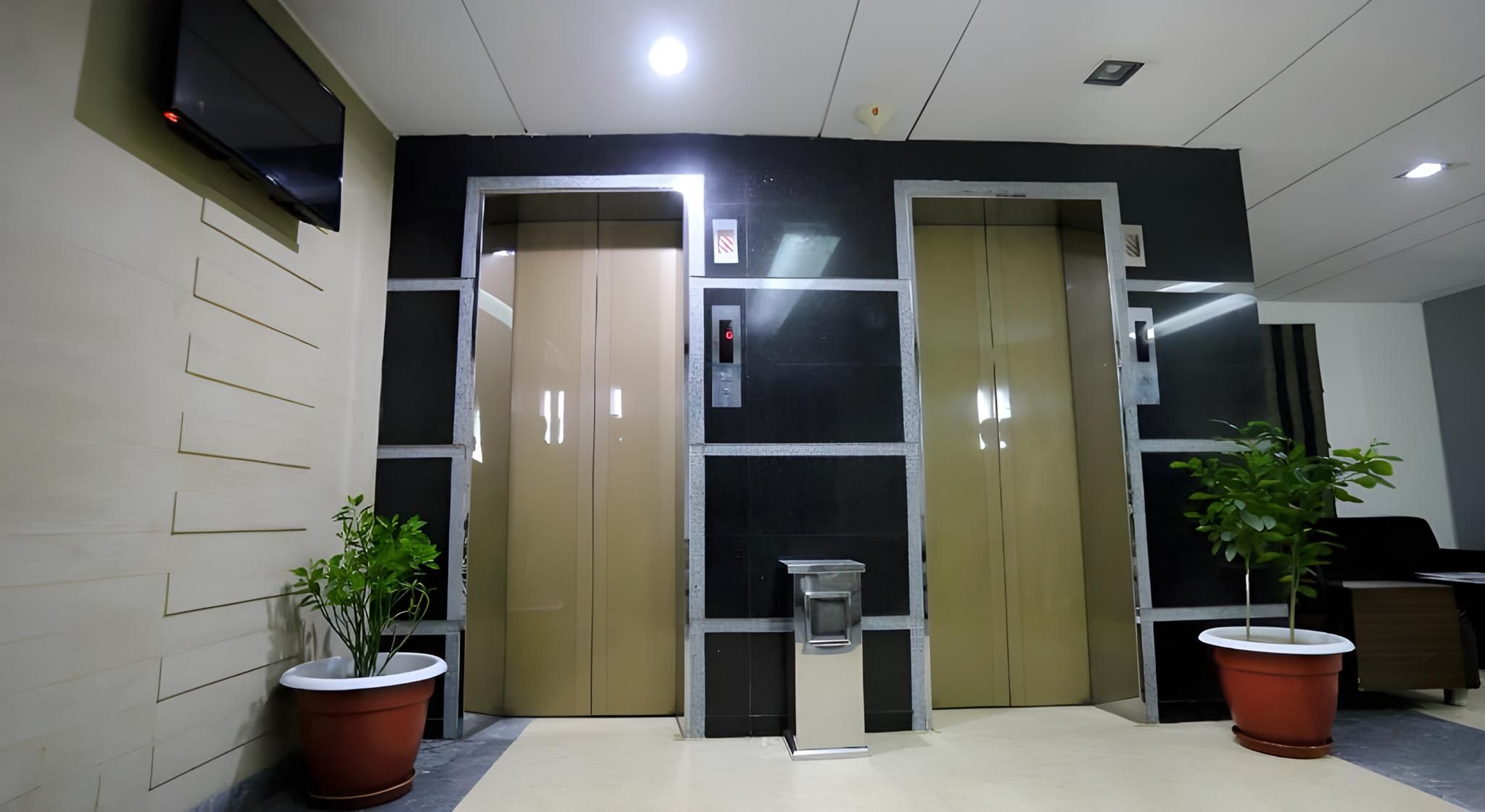 A lobby with two elevators, a reception desk, and potted plants.