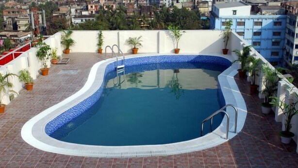 Una piscina en la azotea con borde de azulejos, rodeada de plantas en macetas, con vistas a un paisaje urbano.
