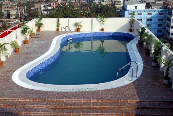 A rooftop swimming pool with a blue tiled edge, surrounded by potted plants and a cityscape view. - Orchid Business Hotel (Chittagong)