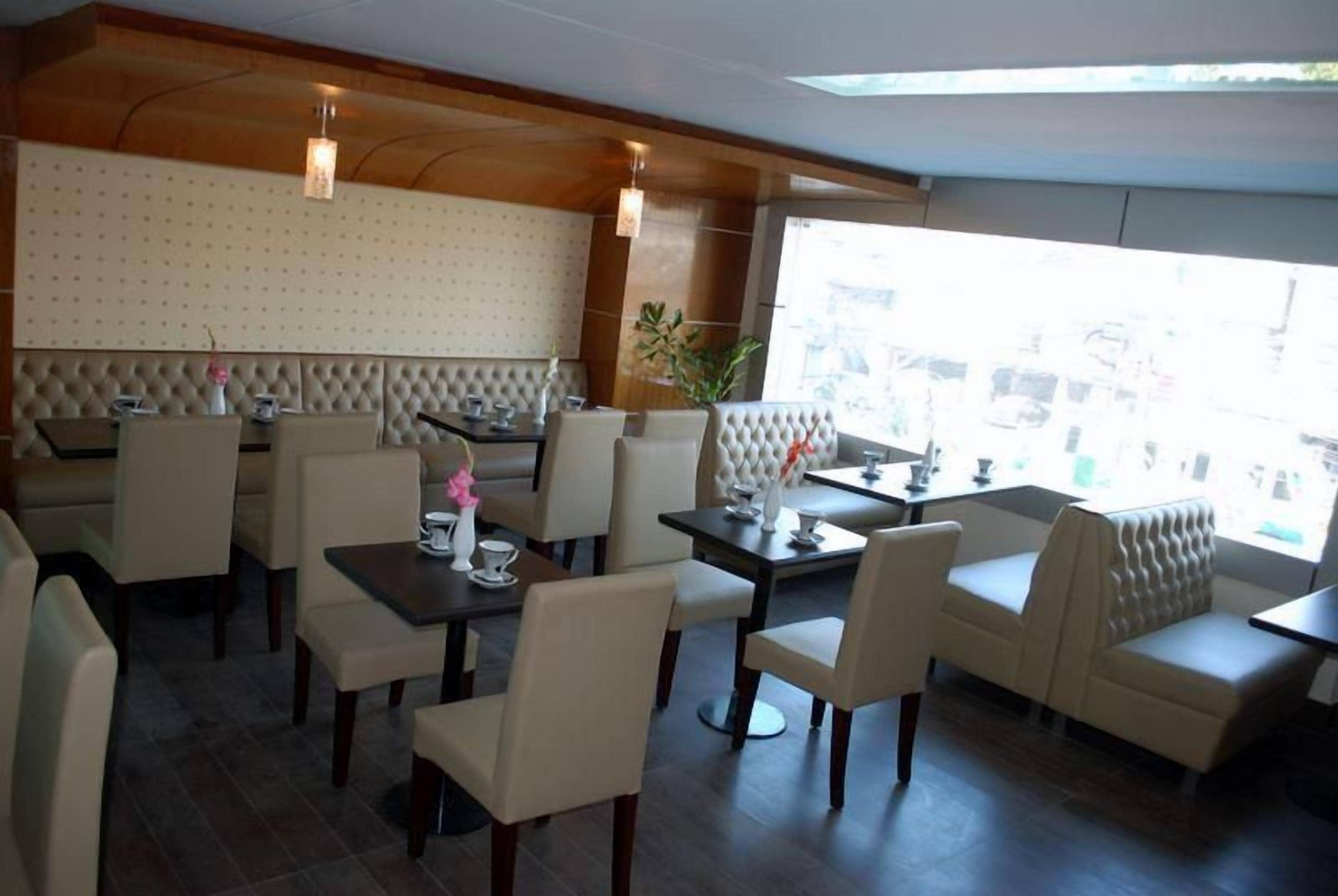 A restaurant with a high ceiling, cushioned seating, and a view through large windows.
