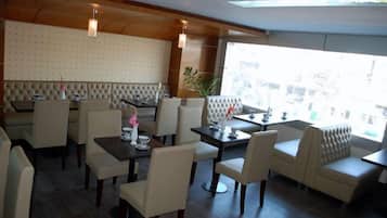 A restaurant with a high ceiling, cushioned seating, and a view through large windows.