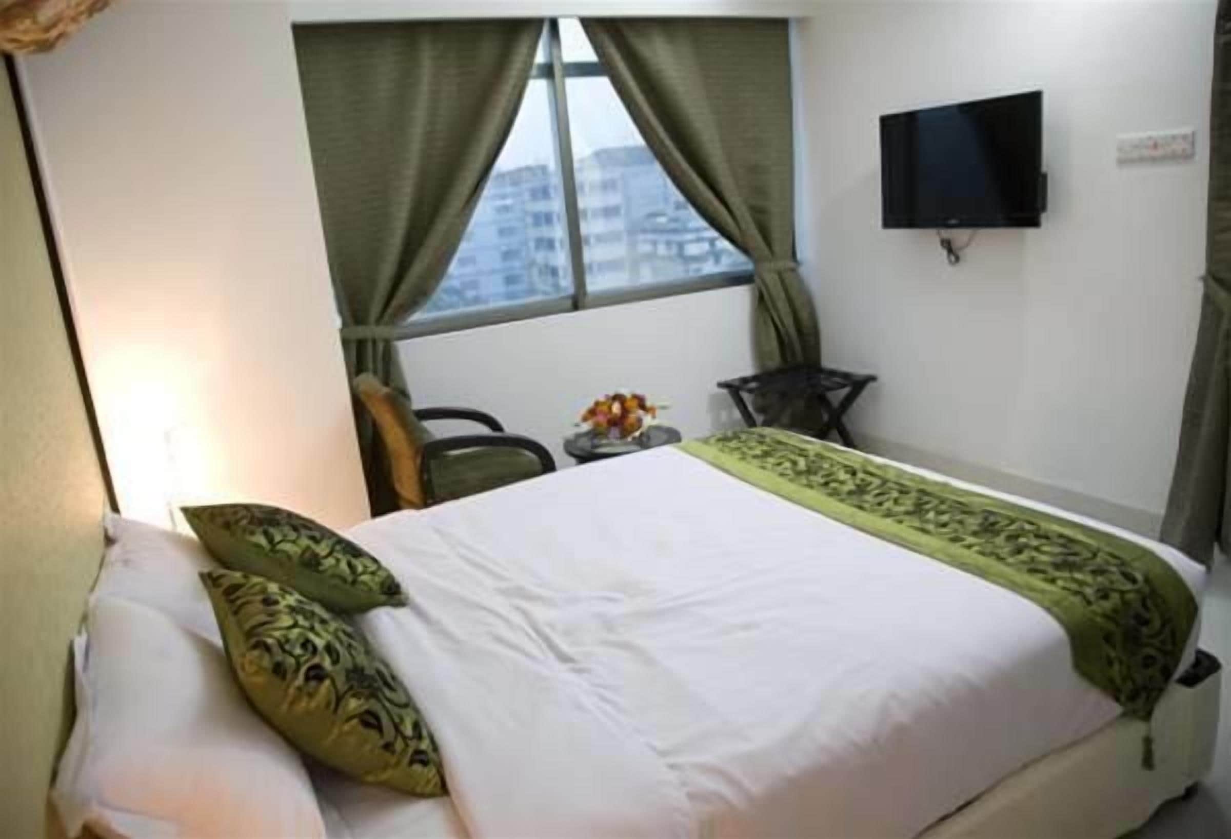 A hotel room with a bed, a television mounted on the wall, and a window with curtains.
