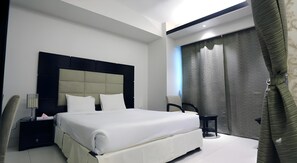 A modern hotel room with a large bed, a bedside table, a chair, and a window with curtains. - Orchid Business Hotel (Chittagong)