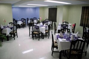 A dining area with tables set for service, chairs, and a blue wall in the background. - Orchid Business Hotel (Chittagong)