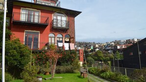 A red two-story house with a balcony, surrounded by greenery and a hillside view. - Lofts Parque Mirador Cerro Alegre (Valparaiso)