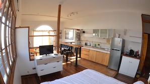 A compact hotel room with a bed, a desk with a TV, a kitchenette, and a large window. - Lofts Parque Mirador Cerro Alegre (Valparaiso)