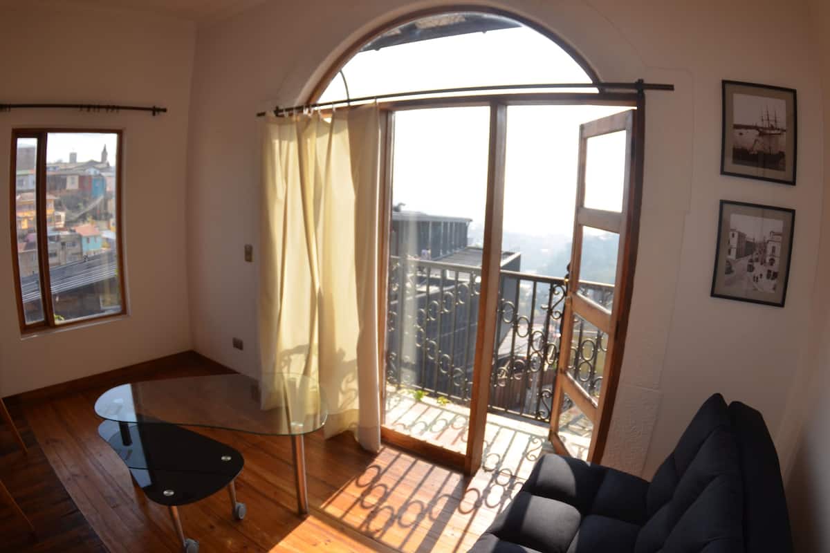 Ein großzügiges Wohnzimmer mit Balkon, großen Fenstern und Blick auf die Stadtlandschaft.