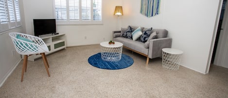A modern living room with a grey sofa, a white TV stand, a blue rug, and a ceiling fan.