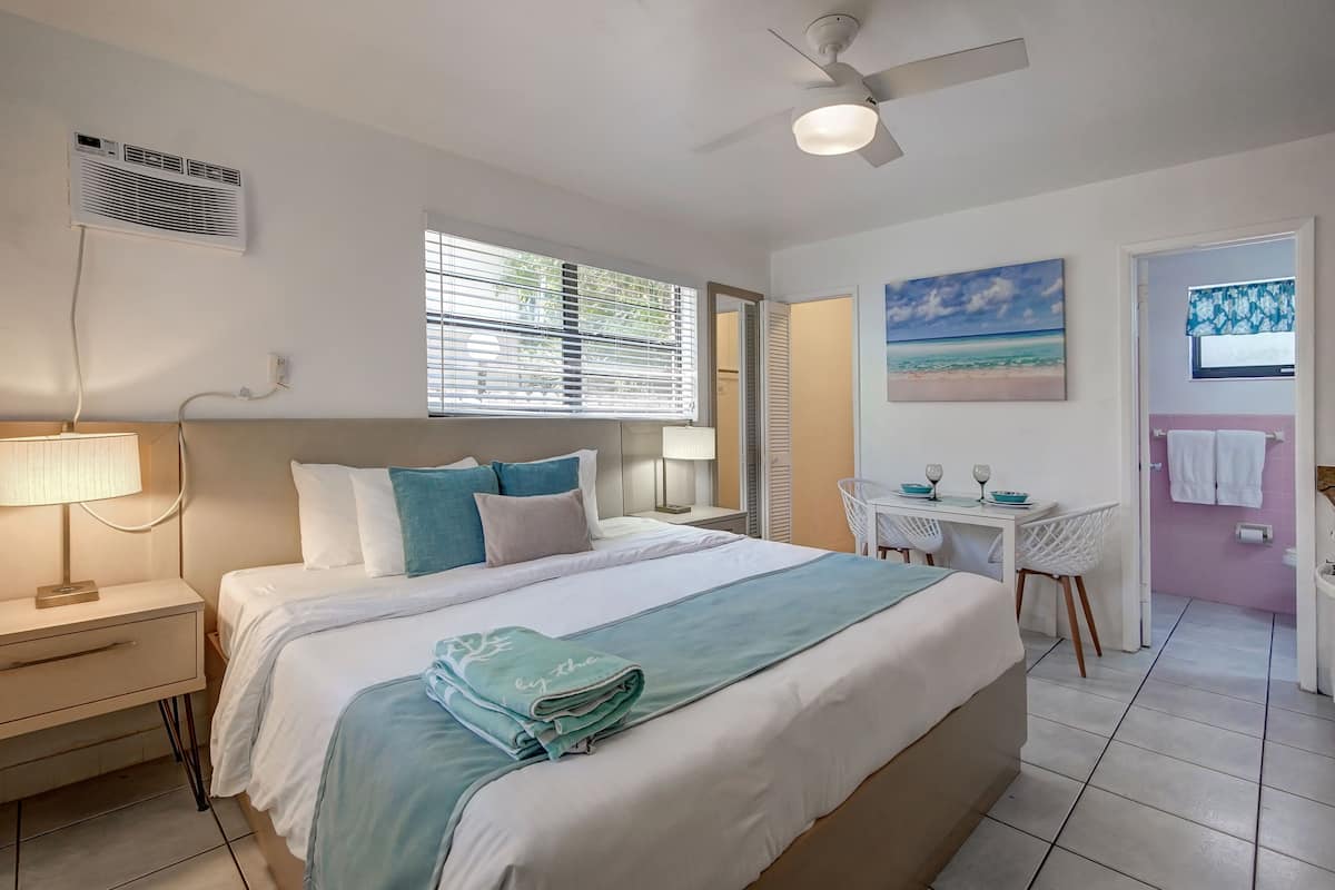 A neatly arranged bedroom with a bed, bedside table, lamp, and a desk with chairs.
