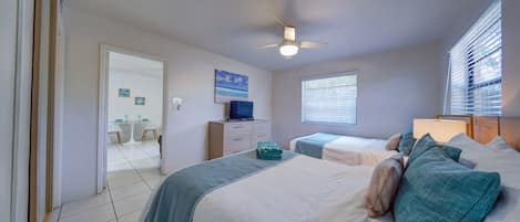 Un dormitorio con dos camas, un ventilador de techo, un televisor y una ventana con persianas.