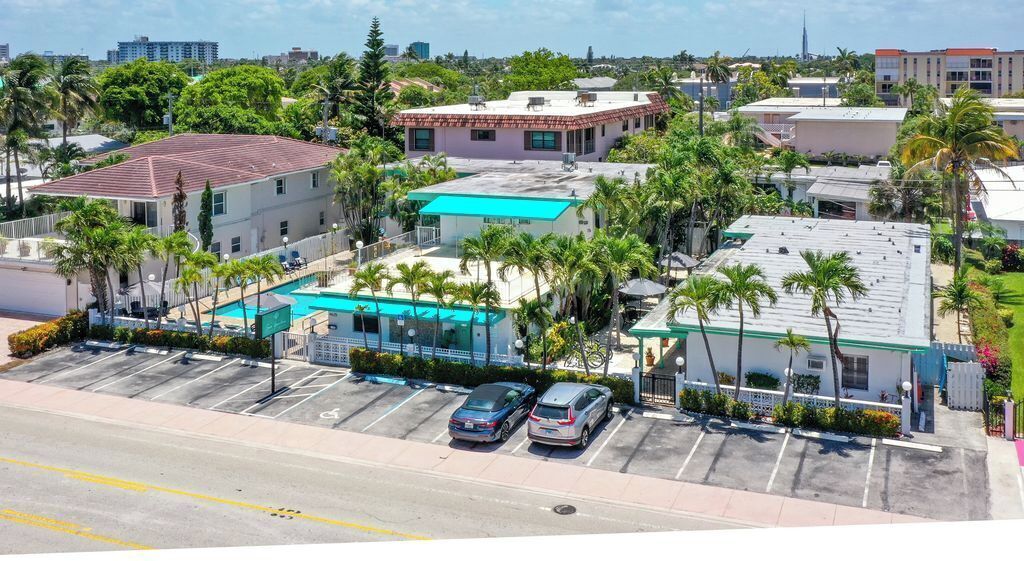A hotel with a swimming pool, parking lot, and surrounding palm trees.