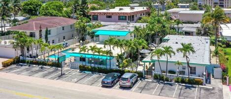 A hotel with a swimming pool, parking lot, and surrounding palm trees.