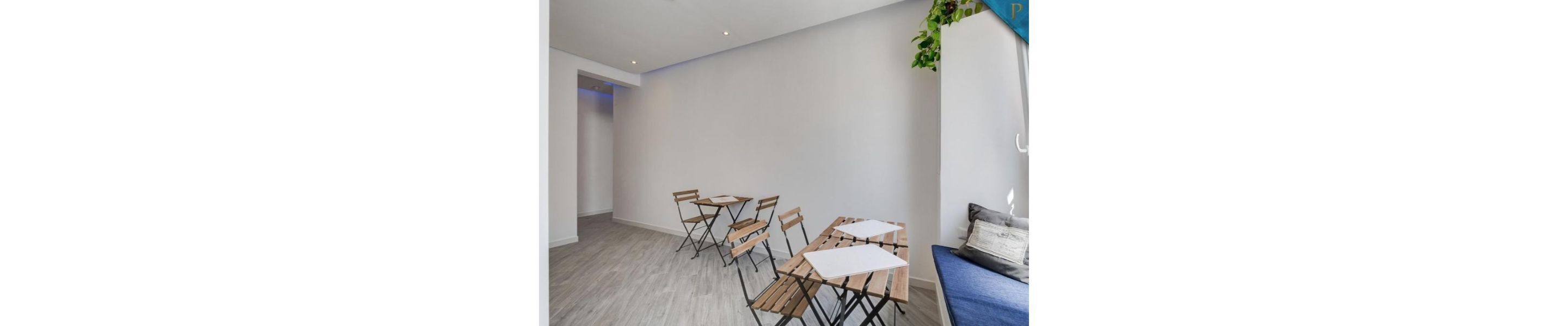 A room with a long table and chairs, a blue sofa, and a plant on the wall.