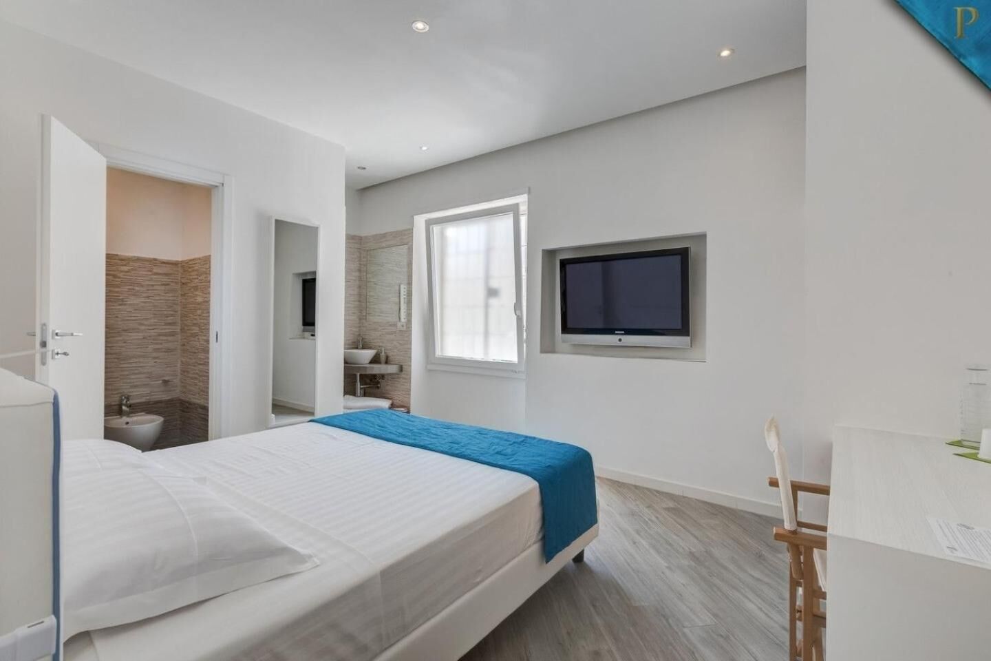 A modern bedroom with a bed, a TV, and a bathroom visible through an open door.