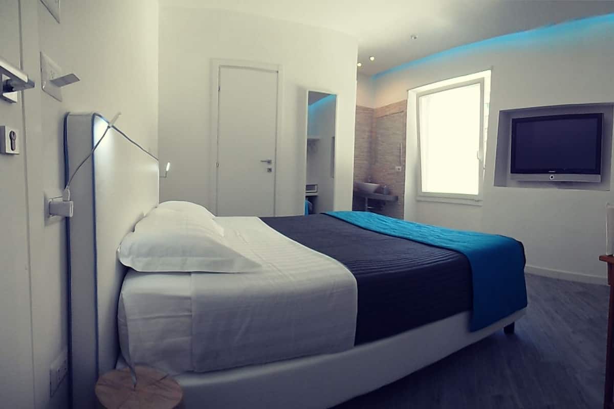 A modern hotel room with a bed, a desk, a TV, and a bathroom visible through an open door.