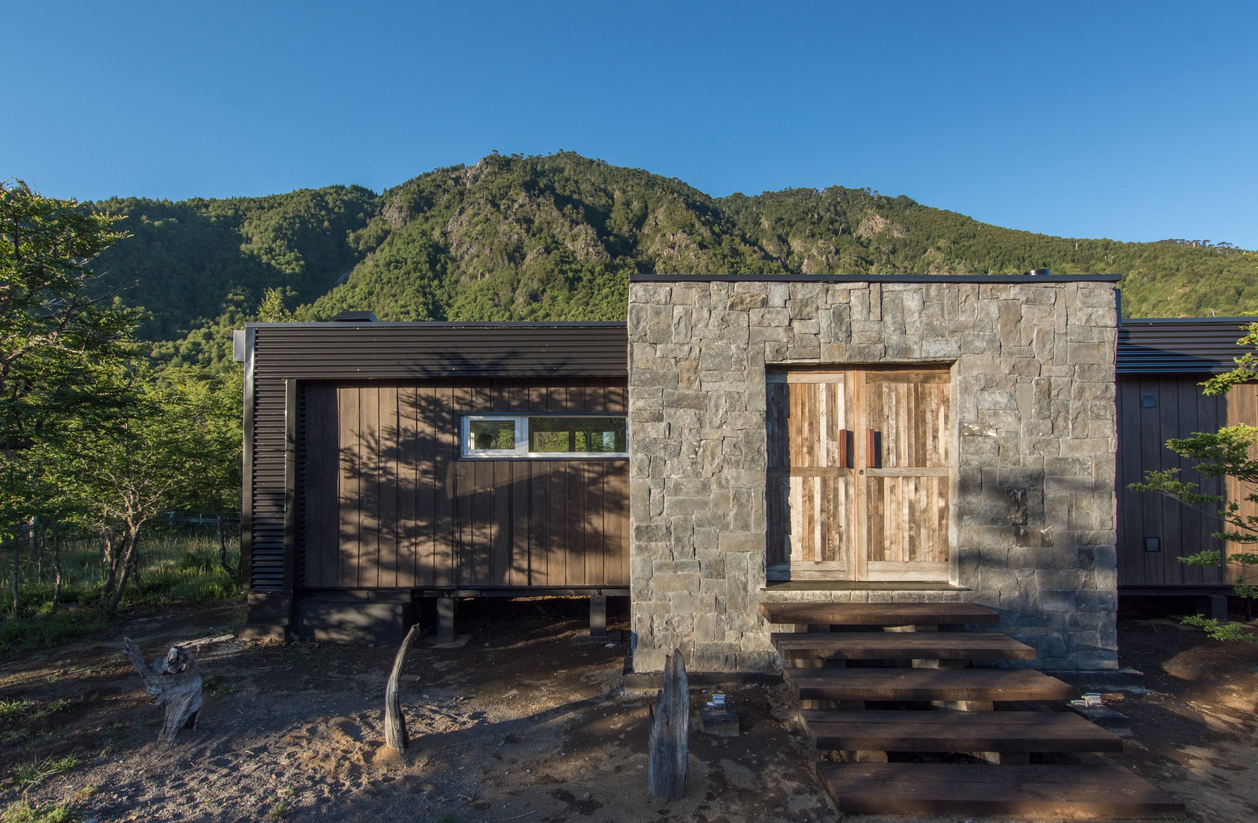 A rustic cabin with a stone entrance, wooden door, and steps leading up to a porch.