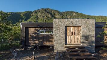 A rustic cabin with a stone entrance, wooden door, and steps leading up to a porch.