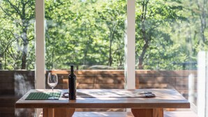 Une table en bois sur laquelle sont posés une bouteille de vin, un verre et des clés, le tout placé devant une fenêtre donnant sur une forêt.