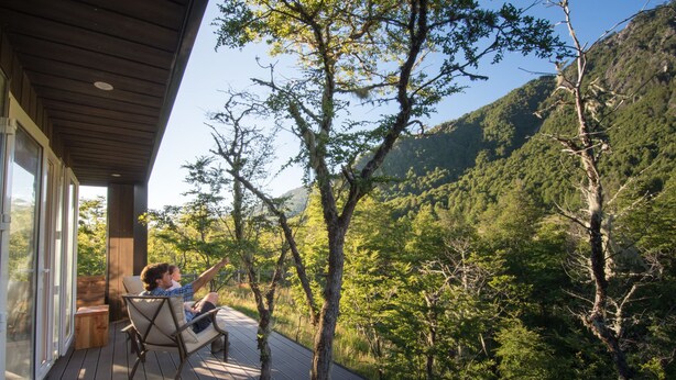 Une terrasse en bois avec un mur de verre donnant sur une colline boisée.