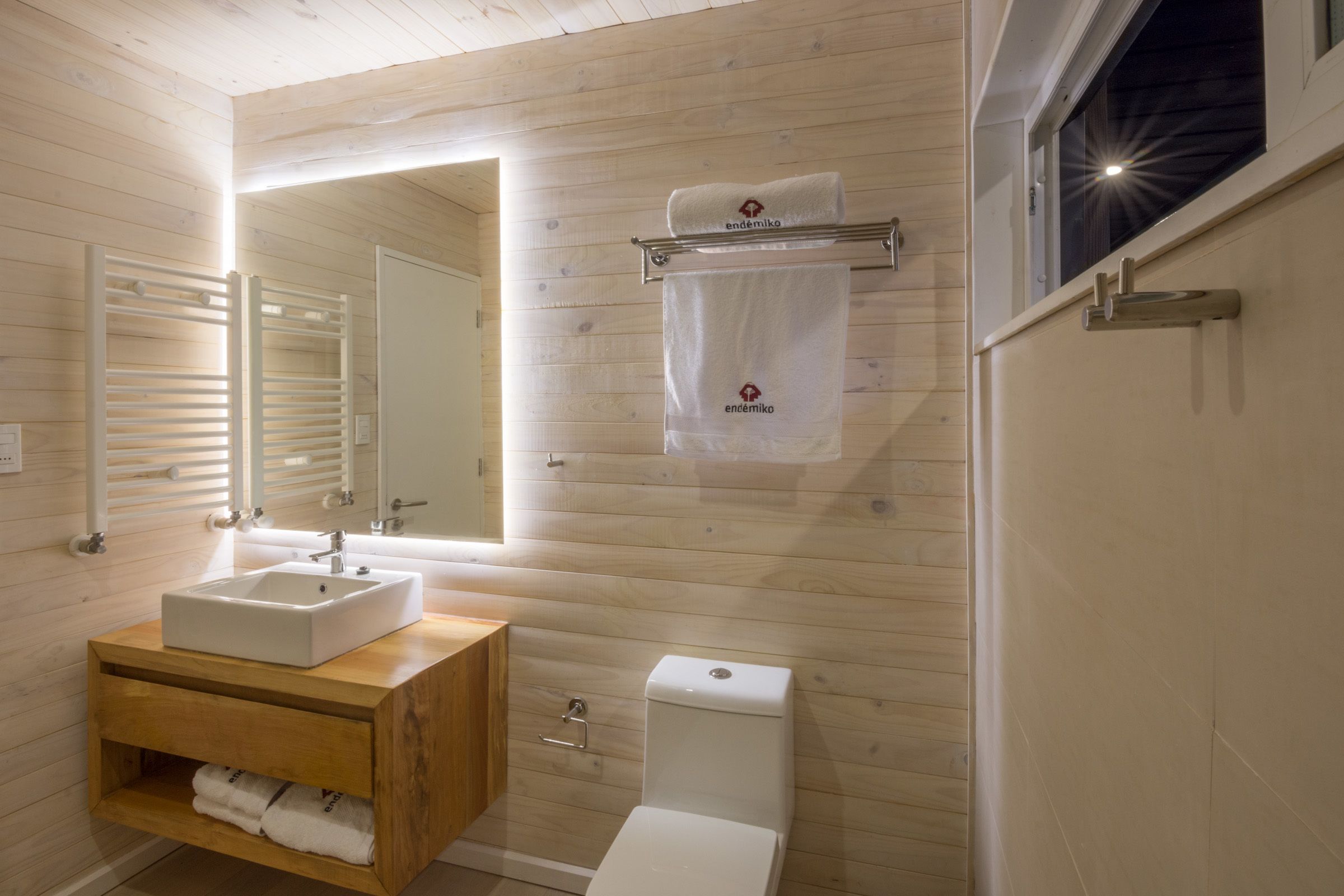 Un baño moderno con paredes de madera, un lavamanos blanco, un inodoro y un perchero con una toalla.