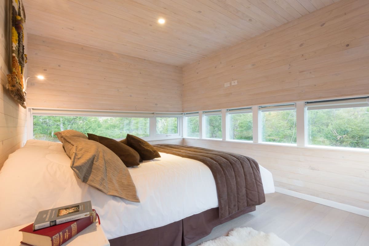 A bedroom with a large bed, multiple windows, and a view of greenery outside.
