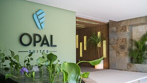 Un espace d’accueil d’hôtel avec une enseigne indiquant « OPAL SUITES » et un élément décoratif aquatique agrémenté de plantes.