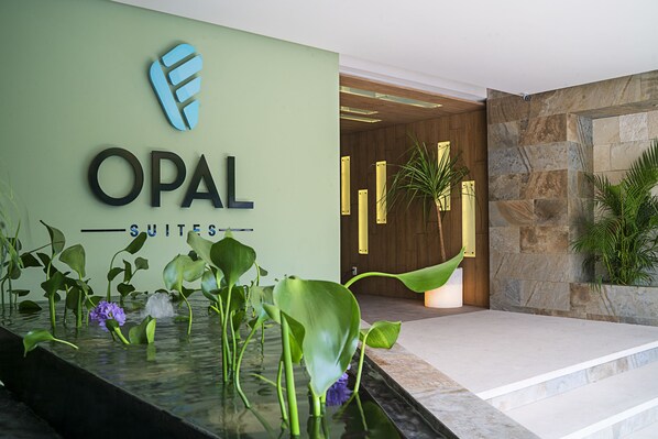 A hotel reception area with a sign reading "OPAL SUITES" and a water feature with plants. - Opal Suites by Homing Bird (Playa del Carmen)