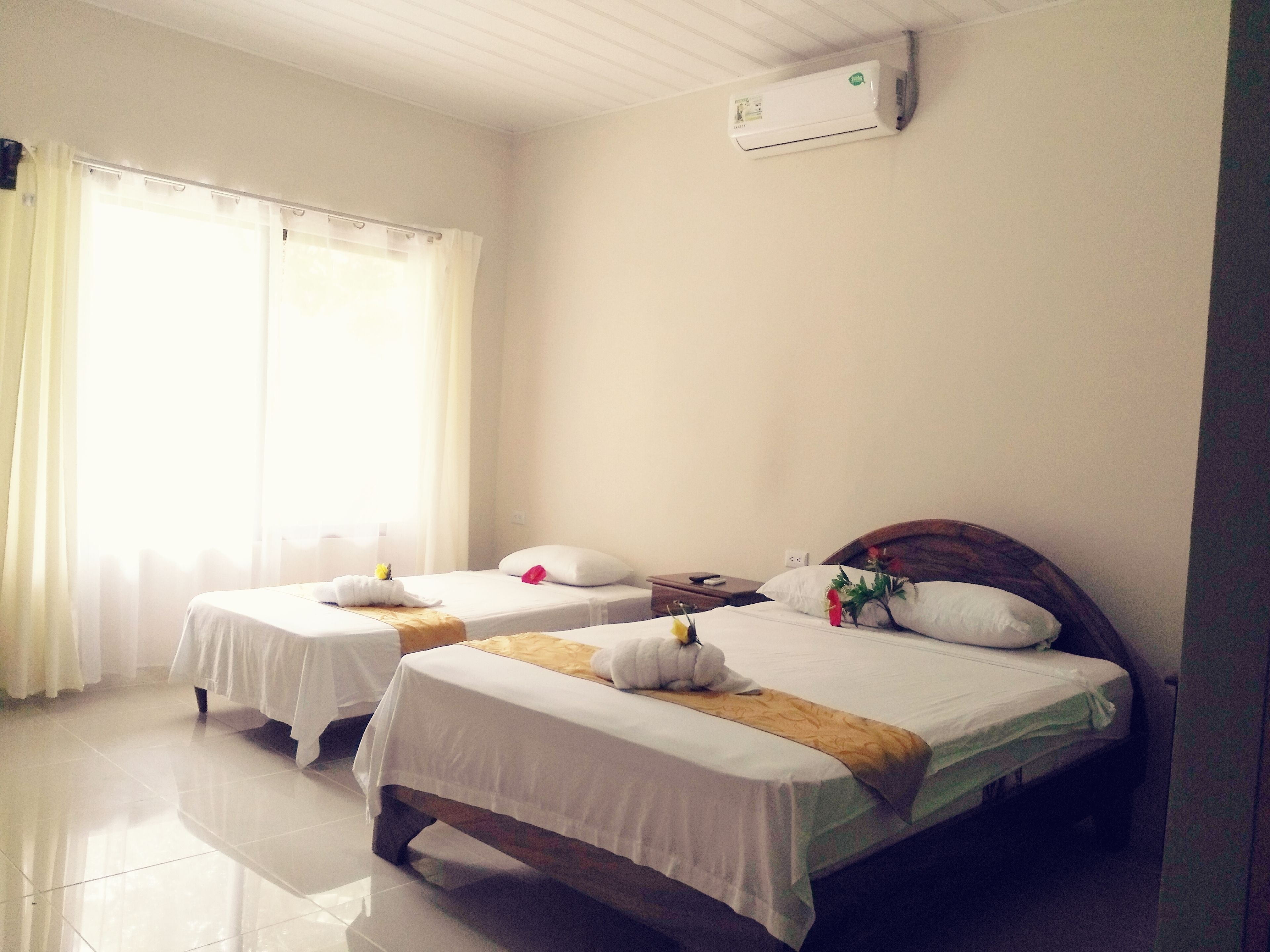 Een hotelkamer met twee eenpersoonsbedden, een houten hoofdbord, een nachtkastje en een airconditioner aan de muur.