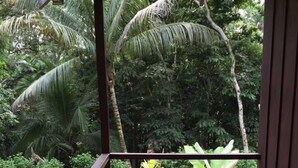 A wooden deck with a table and chairs, overlooking a lush garden with various plants and trees. - Manuel Antonio Hostel Resort (Quepos)