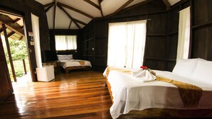 A room with wooden floors, two beds with white linens, a small table, and a white refrigerator. - Manuel Antonio Hostel Resort (Quepos)