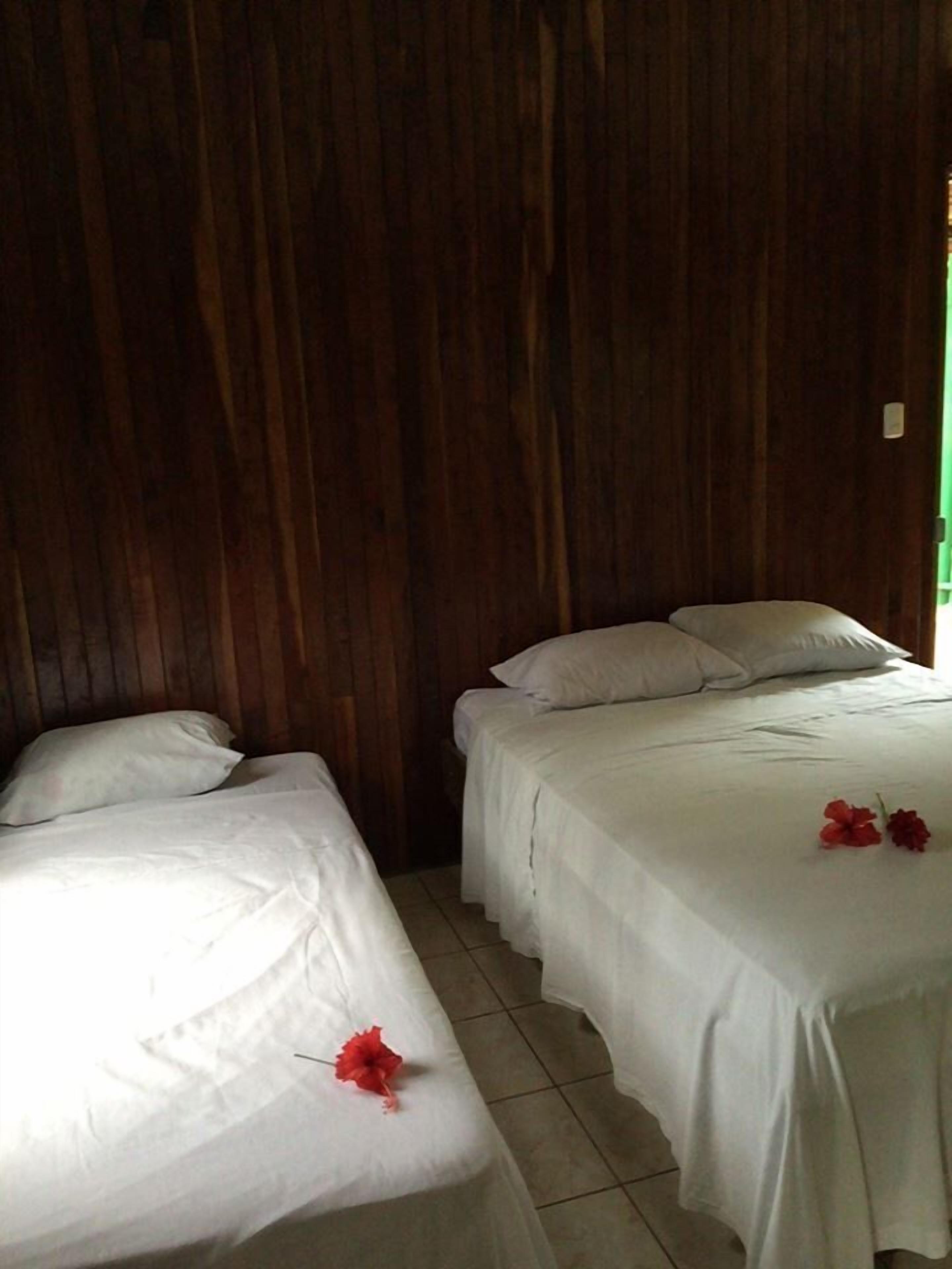 A room with two single beds and a double bed, all with white linens. There are red flowers on the beds.