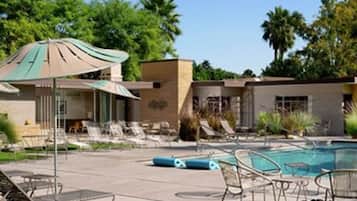 A pool area with lounge chairs and umbrellas, a building with a flat roof, and a well-maintained lawn.