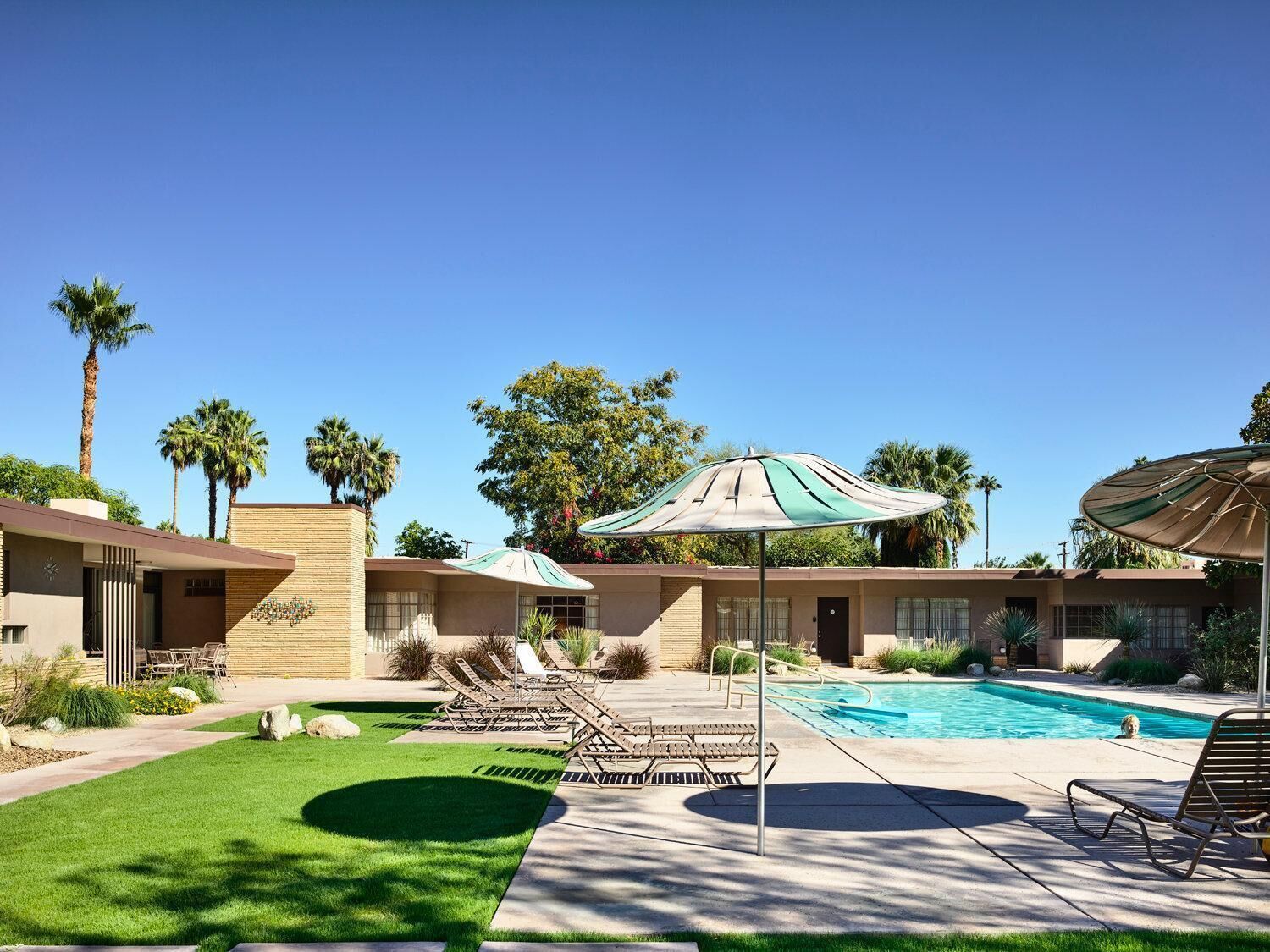 A pool area with lounge chairs, umbrellas, and a clear blue sky.