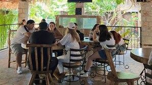A group of people seated at tables under a wooden roof with a television screen mounted above. - Mayan Hills Resort (Copan Ruinas)