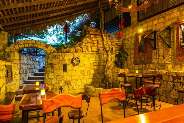 A rustic restaurant with stone walls, wooden tables, and chairs.