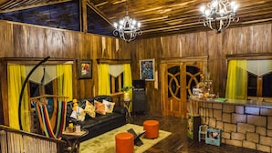 A cozy room with a wooden ceiling, a black leather sofa, orange ottomans, and a small table with a plant. - Mayan Hills Resort (Copan Ruinas)