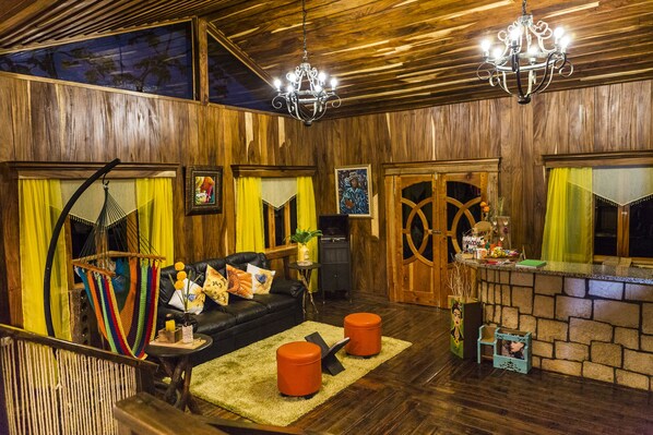A cozy room with a wooden ceiling, a black leather sofa, orange ottomans, and a small table with a plant. - Mayan Hills Resort (Copan Ruinas)