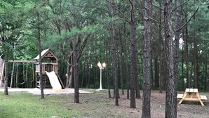 Un parque infantil con tobogán y columpios, rodeado de árboles.