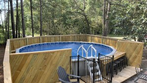 Una terraza de madera con un jacuzzi, dos sillas tipo Adirondack y una mesita.