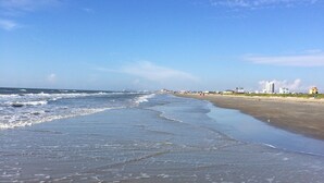 A beach with waves, a clear sky, and buildings in the distance. - East Island Oasis: On the Beach, NO Seawall Blvd, Mins 2 Everything, Pool, WIFI (Galveston)