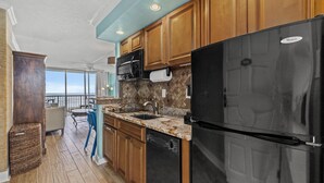 A kitchen with wooden cabinets, a black refrigerator, and a stone backsplash. - East Island Oasis: On the Beach, NO Seawall Blvd, Mins 2 Everything, Pool, WIFI (Galveston)