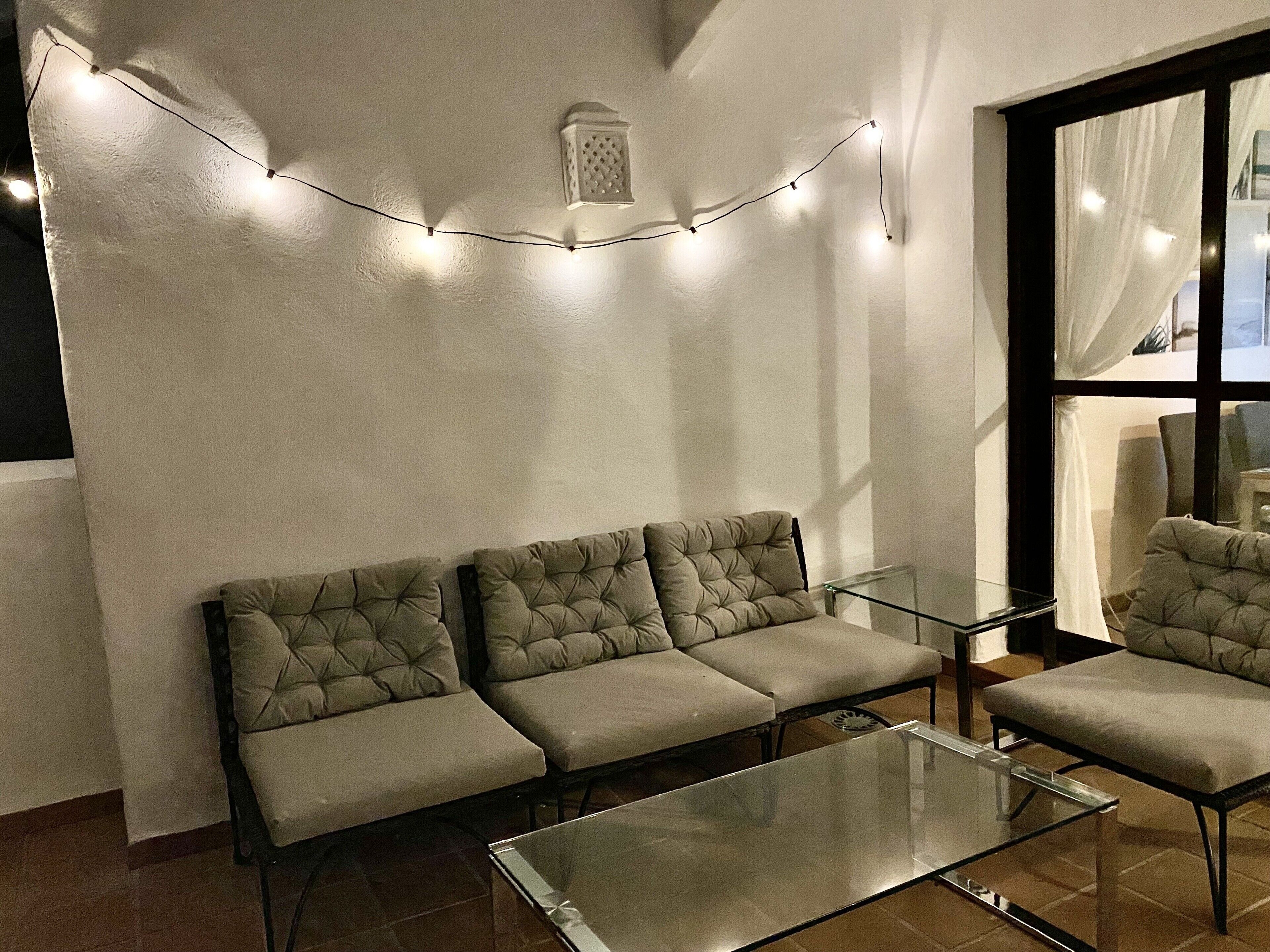 Uma sala de estar moderna com um sofá, uma mesa de centro de vidro e luzes de fada na parede.