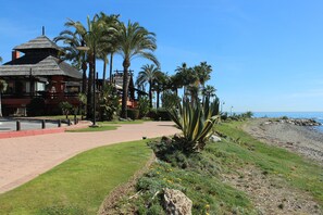 Una propiedad frente a la playa con un paseo empedrado, palmeras y un edificio con techo de paja.