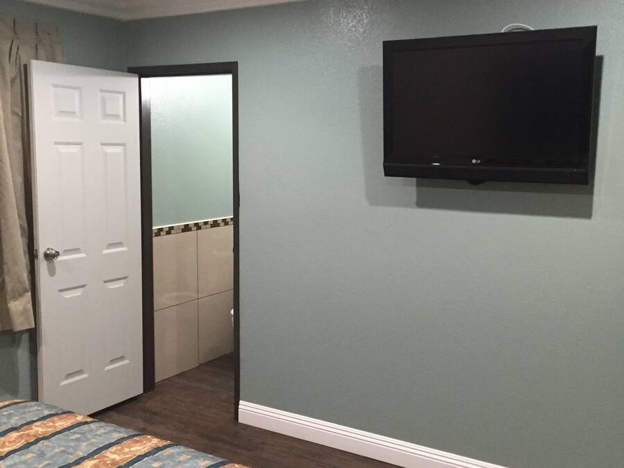 A bedroom with a bed, a television mounted on the wall, and a door leading to a bathroom.