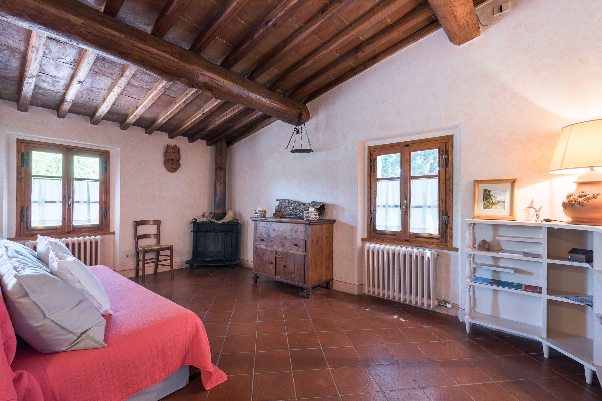 Une chambre avec un plafond en bois, un lit avec une literie rose, une commode et un radiateur.
