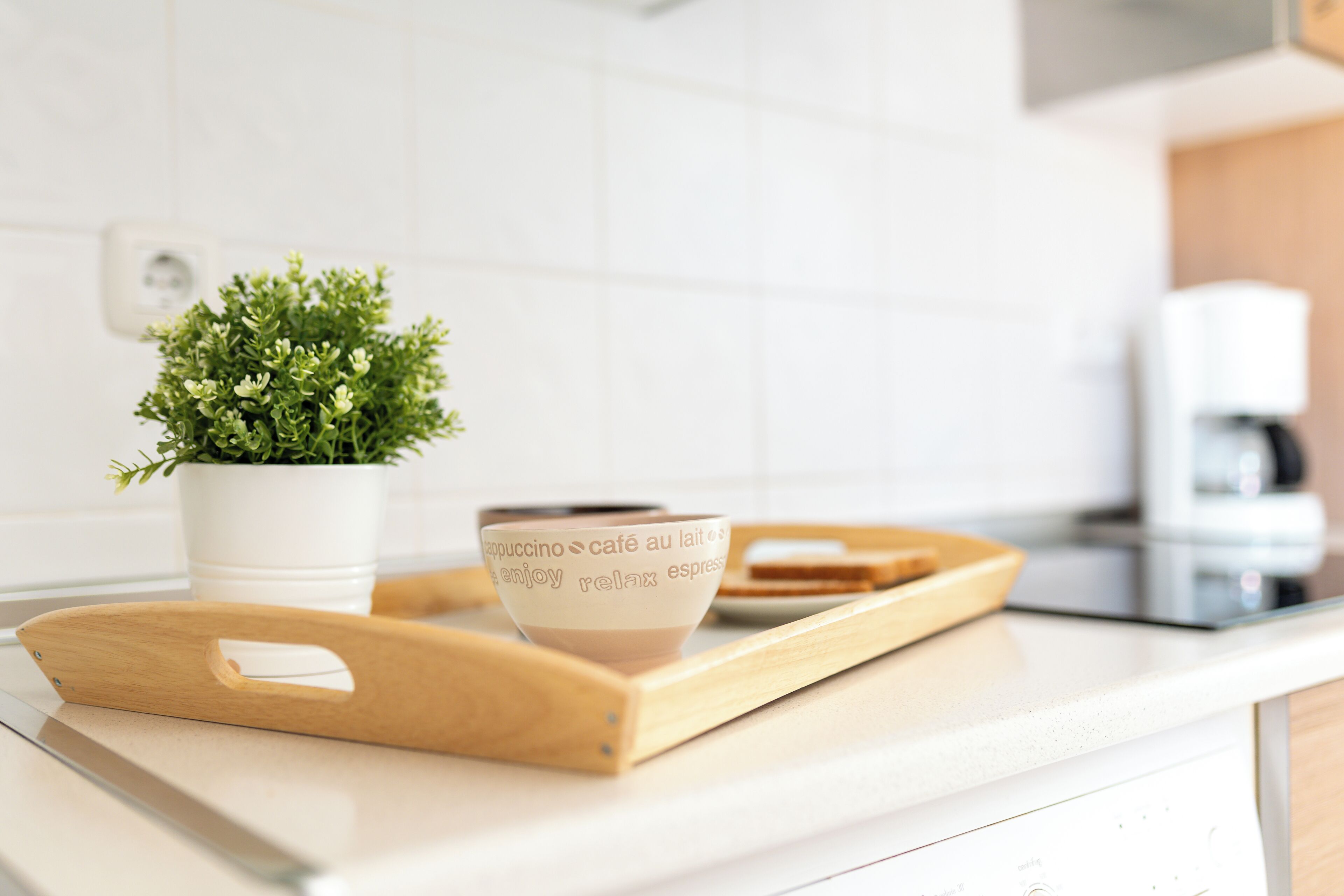 A kitchen counter with a coffee cup, a wooden tray, and a potted plant.