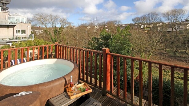 A hot tub on a wooden deck with a view of houses and trees in the background. - Beautiful 19th Century Seaside Cottage with hot tub and river views (Cemaes Bay, Anglesey)