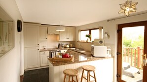 A kitchen with white cabinets, a granite countertop, a built-in oven, a sink, and two wooden stools. - Beautiful 19th Century Seaside Cottage with hot tub and river views (Cemaes Bay, Anglesey)