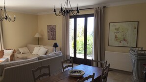 Ein Essbereich mit Holztisch und -stühlen, einer Couch mit Kissen, einer Chandelierleuchtre und einer Karte an der Wand.
