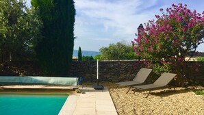 Ein Poolbereich mit einer Steinsäule, zwei Liegestühlen und einer Pergola mit rosa Blumen.
